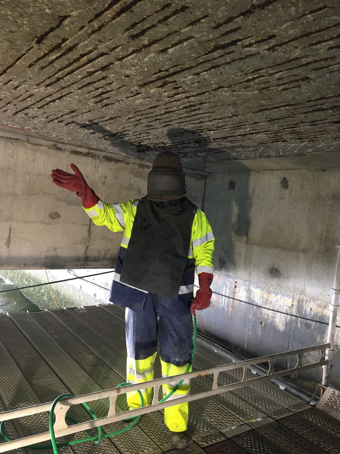 Fagperson i verneutstyr under sandblåsing av frilagt armering på kaikonstruksjon